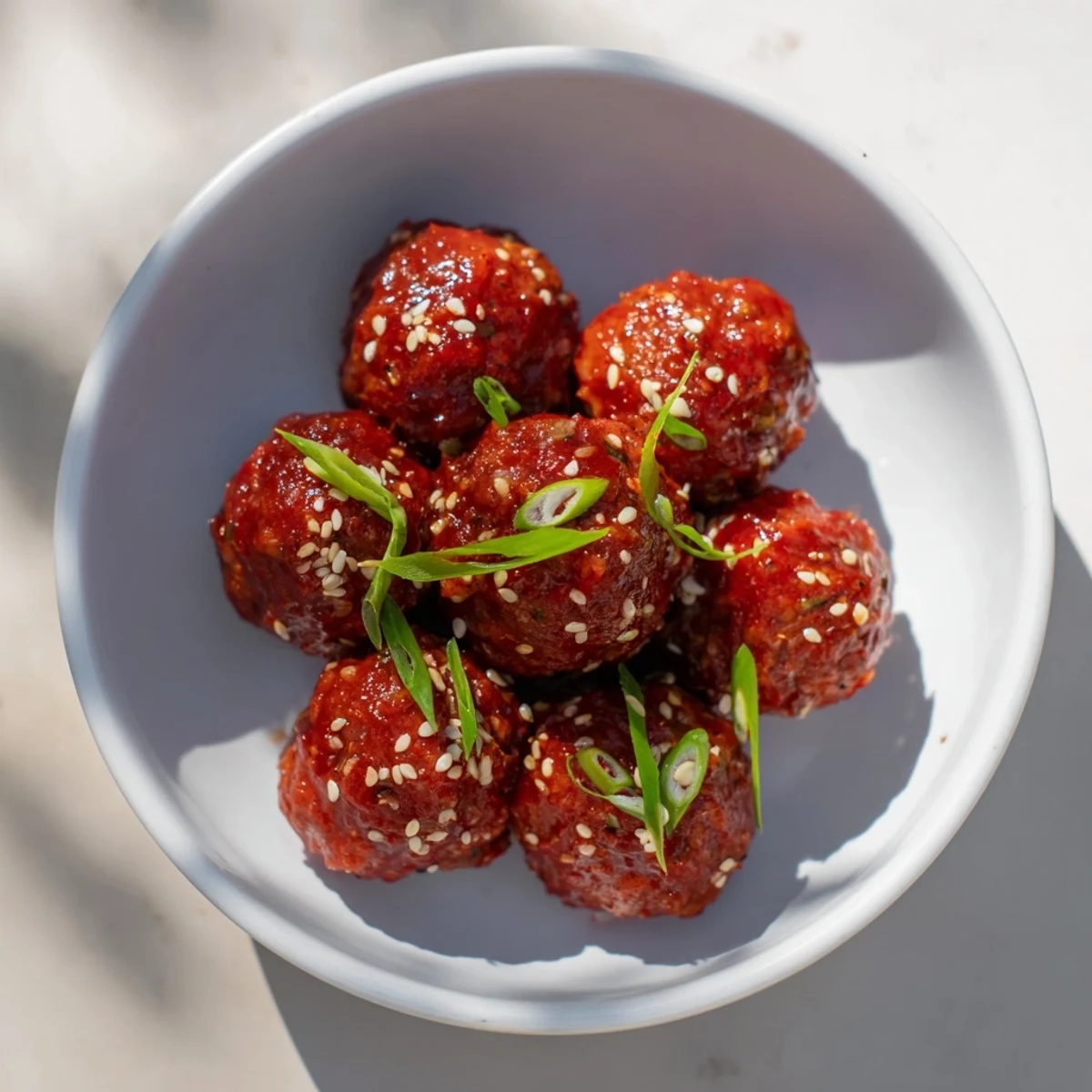 Appealing image of Spicy Sriracha Honey Meatballs, garnished with sesame seeds and green onions.
