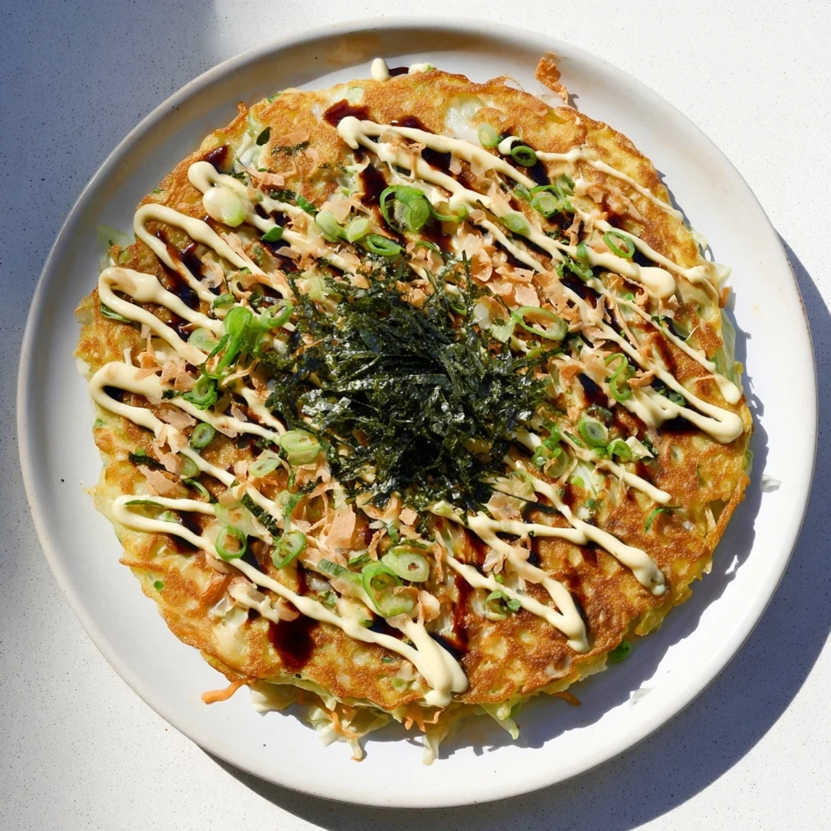 Close-up of golden-brown okonomiyaki pancakes topped generously with sauce and dancing bonito flakes.