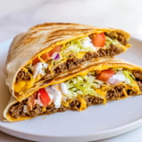 Golden brown Taco Bell Crunchwrap Supreme, with melted cheese and fresh veggies spilling over.
