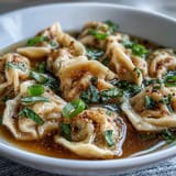 Soft, handmade dumplings float in rich chicken broth, garnished with vibrant scallions for a comforting, aromatic soup perfect for chilly days.  