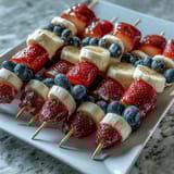 Patriotic red, white, and blue fruit skewers with strawberries, bananas, and blueberries arranged for a festive Fourth of July spread.