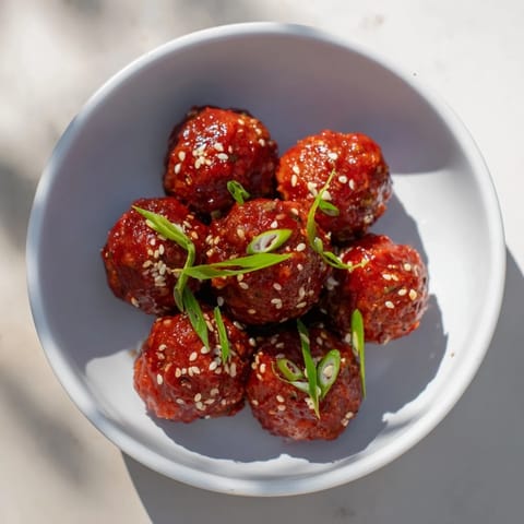 Appealing image of Spicy Sriracha Honey Meatballs, garnished with sesame seeds and green onions.