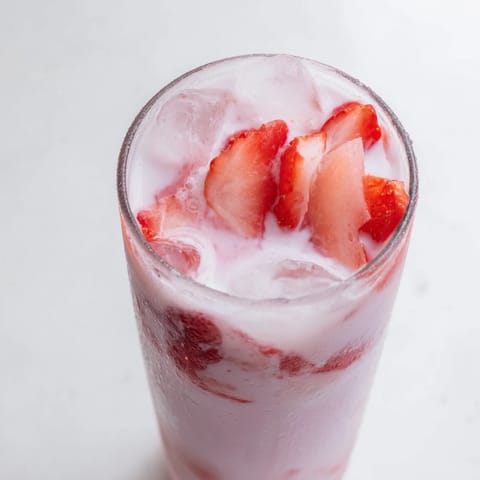 A close-up of the Refresher Copycat Pink Drink in a clear glass, showing its rosy hue and garnished with a fresh strawberry.