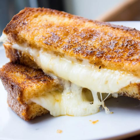 A close-up of a Three-Cheese Grilled Cheese, showing a crispy, buttery crust and melted cheese pull from the skillet.