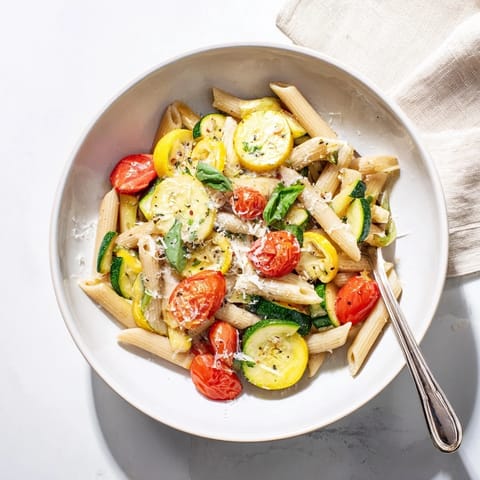 Steaming Garden Veggie Pasta in a white bowl, showcasing vibrant yellow squash, zucchini, and blistered cherry tomatoes.  
