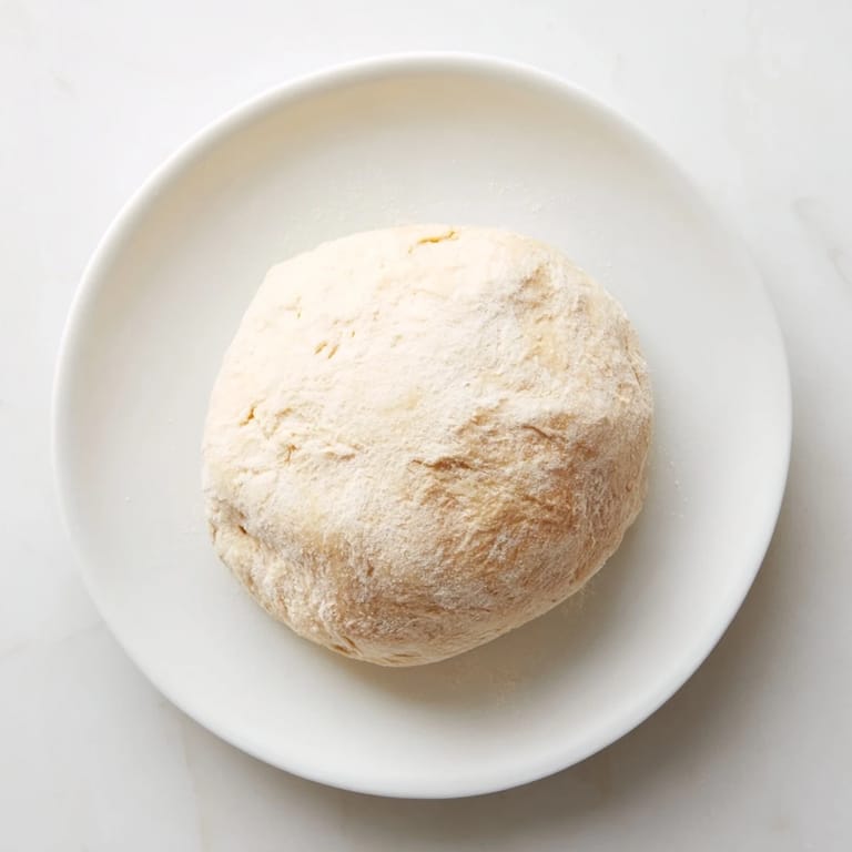 Warm, soft homemade pizza dough, shaped and ready for toppings, perfect for Italian night.