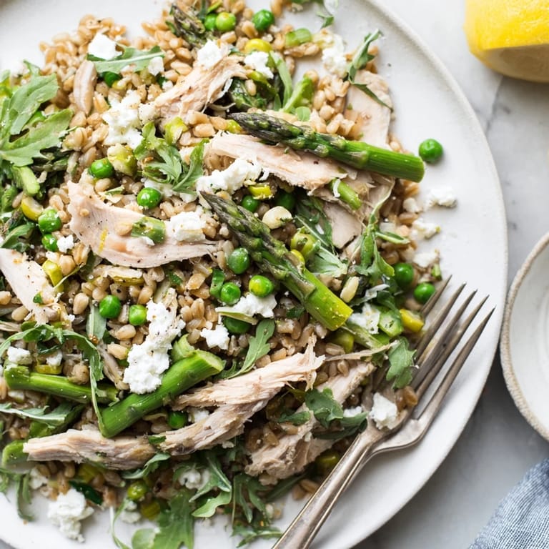 A vibrant bowl of wholesome farro salad with juicy sliced chicken, blanched vegetables, and a light lemon dressing.