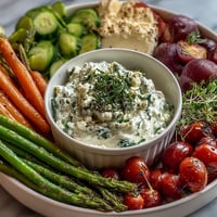Vibrant spring vegetable platter with radishes, peas, and herb dip on a rustic wooden board.