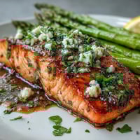 Garlic Butter Salmon with Asparagus sizzling in a skillet, topped with fresh herbs and lemon slices for a vibrant spring meal.